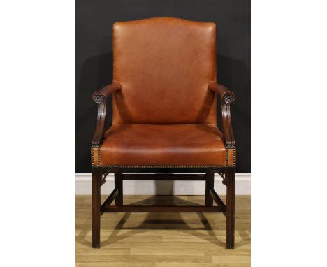 A Chippendale Revival mahogany Gainsborough armchair, stuffed-over leather upholstery, the hand rests carved with a flower he