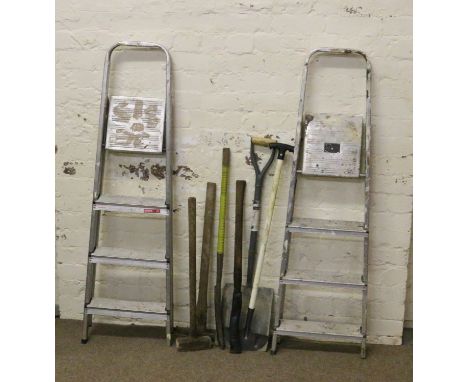 Two pairs of aluminium step ladders along with a collection of garden tools.