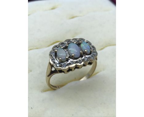 A 9ct gold ladies ring set with three opal stones and surrounded by diamonds, Size N. 