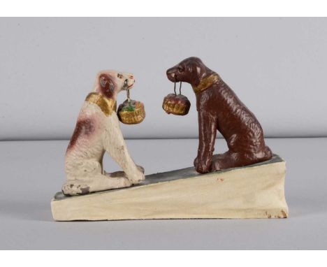 A late 19th century Thüringen seated dogs holding baskets squeak toy, composition seated dogs, one painted white with brown p