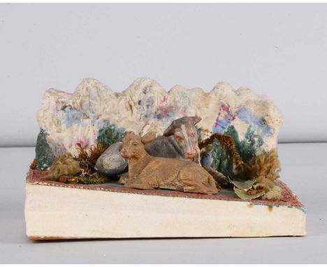 A late 19th century Thüringen cow and calf squeak toy, composition lying cow and calf with rocky backdrop, applied foliage, D