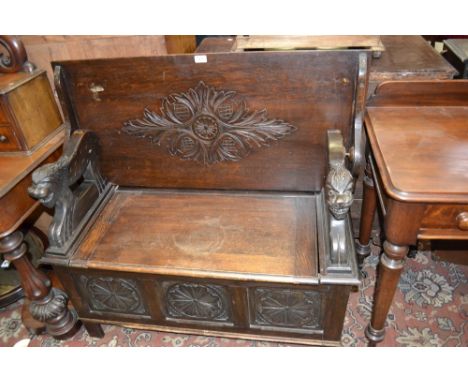 An oak monk's bench, carved top, open arms lion mask terminals, three carved panels to front, circa 1910.