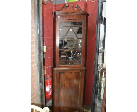 A mahogany floor standing corner cabinet, broken swan neck pediment. gilt metal griffin finial, canted angles, astragal glaze