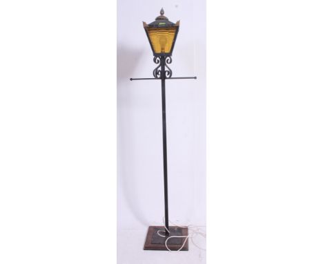 A decorative cast metal lamp standard in the form of a street light having yellow glass shade. Set on wooden plinth .H175 x W