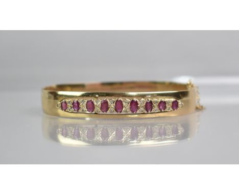 A Ruby and Diamond Set 9ct Gold Hinged Bangle, Nine Graduated Oval Cut Rubies, Largest 5.1mm by 2.8mm, with Eighteen Round Cu