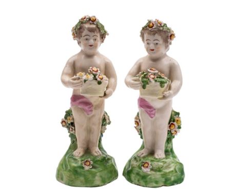 Two Derby figures of putti: each holding a basket of flowers, on green mound bases, patch marks, late 18th century, 16cm [one