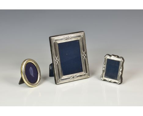 Three modern silver easel back photo frames, the largest of rectangular form with stylised raised decoration to rim and blue 
