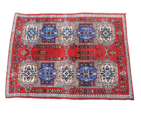 A Moroccan Agadir wool rug, late 20th century, with two rows of five ivory and royal blue medallions on a red field with tree