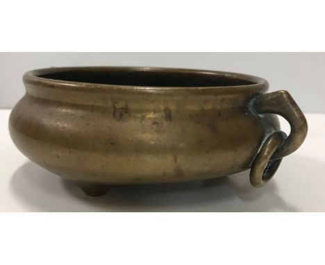 A Chinese bronze censer of small proportions, the squat bellied body with integral brass ring handles raised on three squat f