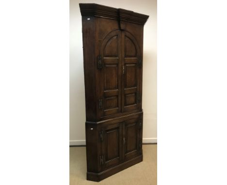 A late 18th/early 19th Century oak free standing corner cupboard with two arched fielded panelled doors enclosing two shaped 