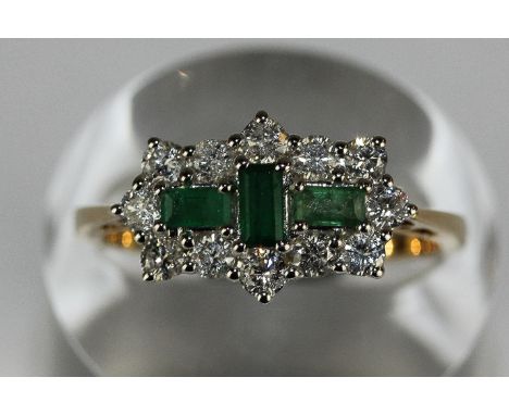 An emerald and diamond ring set with three baguette emeralds within a border of twelve round brilliant cuts in 18ct white and