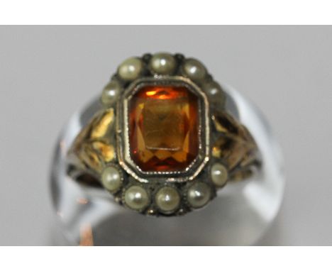 A citrine and pearl ring the step cut stone rubover set within a ten pearl border on a white and yellow metal mount 