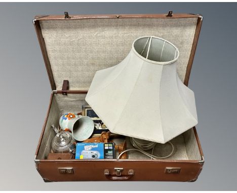 A vintage luggage case containing cameras, a plated teapot, china dog figures, Denby table lamp with shade.