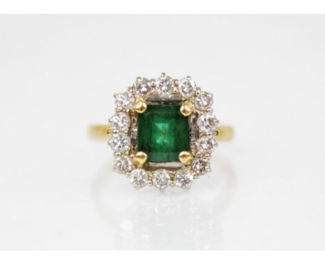 An emerald and diamond 18ct gold cluster ring, the central rectangular step cut emerald measuring 6.88mm x 6.20mm x 4.50mm, c