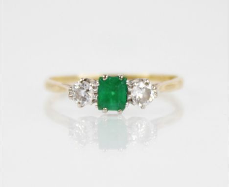 An emerald and diamond three stone ring, the central rectangular step cut emerald measuring 4.5mm x 3.5mm x 3.0mm, with a bri