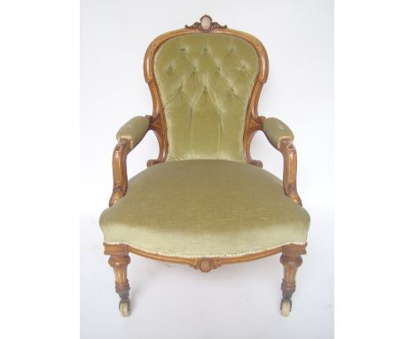 A Victorian buttonback upholstered walnut armchair with moulded and carved frame and padded arms, on turned tapering forelegs