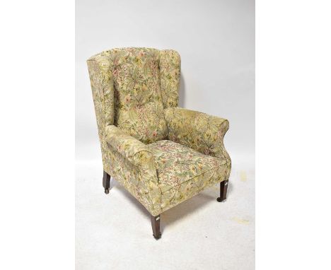 A Georgian-style mahogany wing-back armchair on square tapering legs, with castors, upholstered in a tapestry-style floral fa