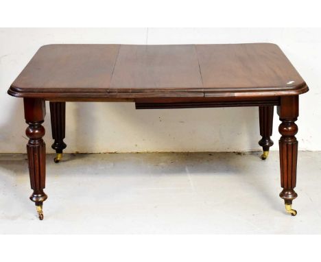A Victorian mahogany wind-out rounded rectangular dining table, with single additional leaf, on reeded supports to brass caps