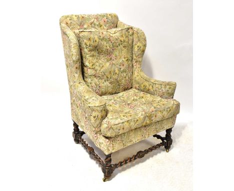 A Georgian-style oak framed wing back armchair, with barleytwist legs and stretchers, on block feet with castors, upholstered
