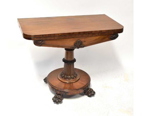 A Georgian mahogany fold-over card table, with carved apron, on a fluted and carved column, to circular base with four lion p
