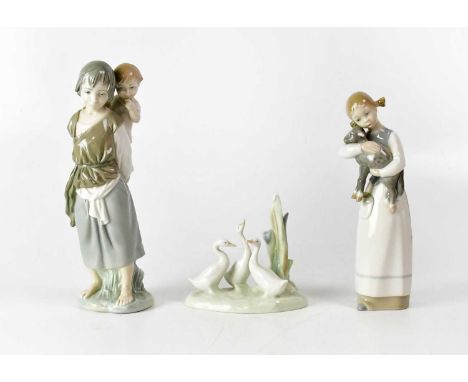 LLADRÓ; two figures comprising a child with a toddler on her back and a girl carrying a lamb, together with a Nao group of th