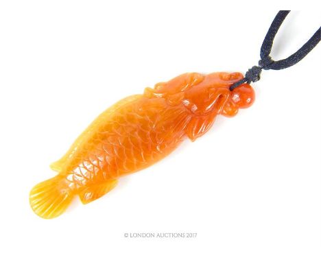 A late 19th century intricately carved orange- coloured jade pendant on an adjustable black silk thong, depicting a scaled ca