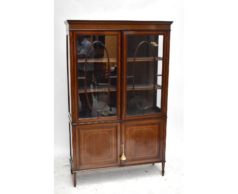 An Edwardian line inlaid mahogany twin door display cabinet, the twin astragal glazed doors enclosing two fitted shelves, rai