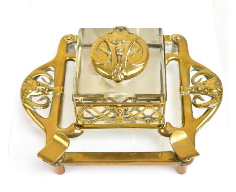 A late 19th/early 20th century German brass mounted clear glass inkwell featuring satyr masks and floral swags, on square sta