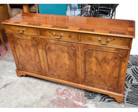 A reproduction yew wood sideboard with crossbanded top above three short drawers and three cupboard doors, on ogee bracket fe