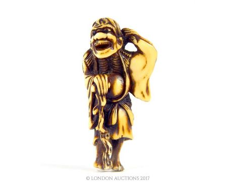 A late 18th / early 19th century carved ivory Japanese netsuke in the form of a demon pulling at his hair, leaning against a 