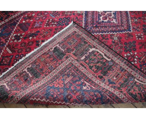 A Caucasian wool carpet, worked with a foliate panel design against a red ground, 310cm x 209cm