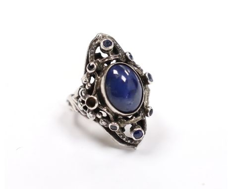 An Arts &amp; Crafts pierced white metal and blue cabochon set dress ring, bordered with seven (ex 8) blue stones, size M.