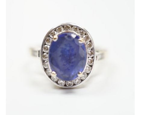 A modern 750 and oval cut single stone tanzanite(worn) set dress ring, with diamond set border and shoulders, size P, gross w