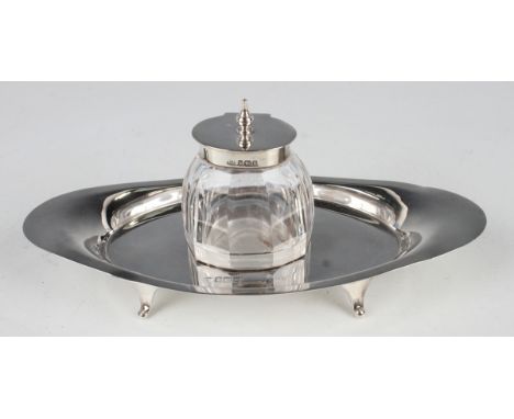 An Edwardian silver and cut glass inkstand, the central facet cut oval inkwell with silver collar and hinged lid, on a boat-s
