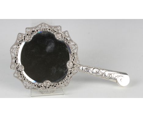 A Victorian silver mounted hand mirror with bevelled circular mirror plate within a cast and pierced floral surround with bea