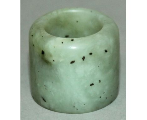 A CHINESE CELADON JADE-LIKE ARCHER’S RING, the stone with darker speckled inclusions, 1.3in diameter & 1.1in long.