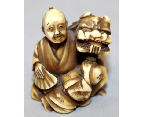A 19TH/20TH CENTURY CARVED &amp; STAINED IVORY NETSUKE OF A MAN &amp; BOY, in the company of a buddhistic lion, 1.5in high.