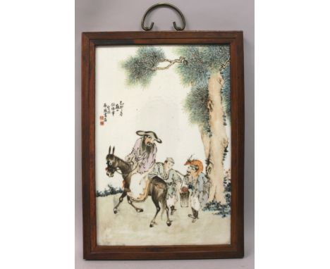 A CHINESE HARDWOOD FRAMED PORCELAIN PANEL, decorated with calligraphy and a group of travellers beneath a pine tree, 16.4in x