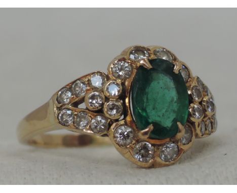 A lady's dress ring having an oval emerald, approx 1ct within a border and open shoulders set with diamond chips, total appro