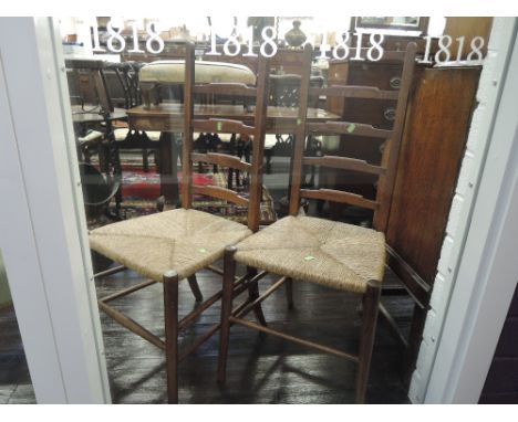 A pair of early 20th century oak ladder back kitchen chairs having later rush seats