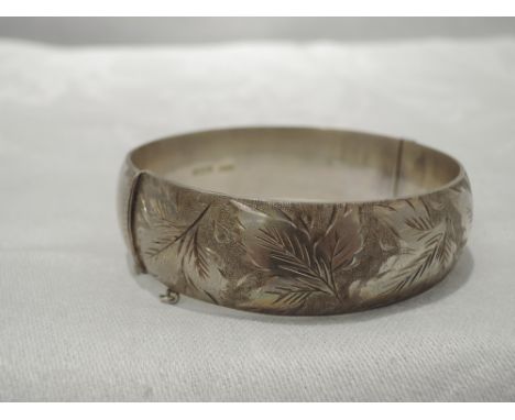 An HM silver hinged bangle of curved form having foliate engraving