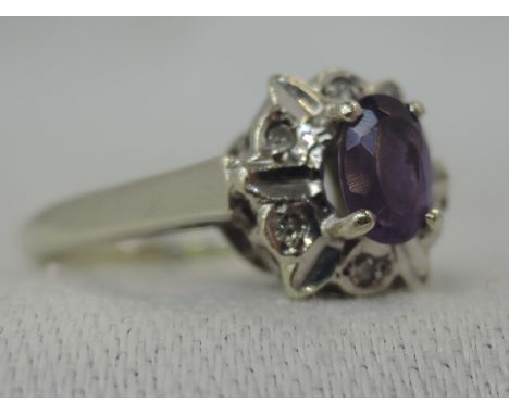 A lady's dress ring having an amethyst style oval stone and diamond chip cluster in an illusionary mount on a 9ct white gold 