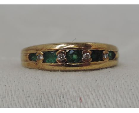 A lady's  eternity ring having five graduated emeralds interspersed by four diamonds in a channel and collared mount on a 9ct