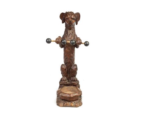 A 19TH CENTURY BLACK FOREST CARVED WALNUT STICK STAND FORMED AS A SEATED DOG holding a bobbin turned stick and mounted on a n