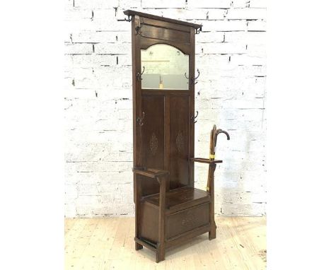 An early 20th century oak hall stand, the panelled mirror back with seven coat hooks over two stick recesses and a hinged sea