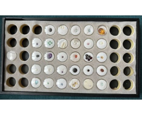 A number of loose gemstones housed in a display case. Includes emerald, tourmaline, opal, aquamarine, fire opal, garnet, amet