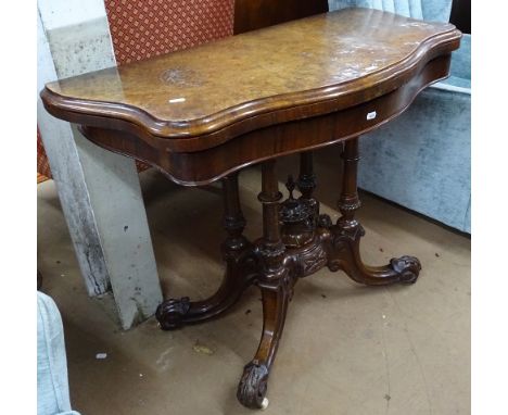 A Victorian burr-walnut topped serpentine fold over card table, raised on a carved quadruple column and sabre leg base, W93cm