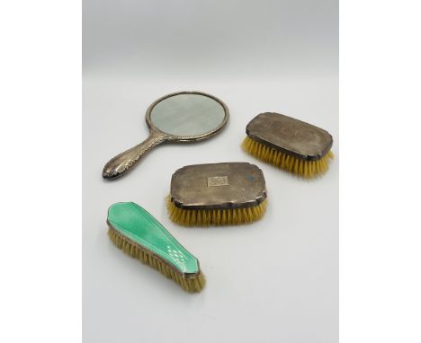 A silver backed hand mirror; two engine turned silver backed brushes (one as found); together with a silver and enamel backed