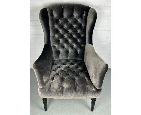 JOHN SANKEY: A WINGBACK ARMCHAIR ON FOUR EBONISED LEGS UPHOLSTERED IN BUTTON BACK VELVET FABRIC,114cm x 77cm x 70cm 