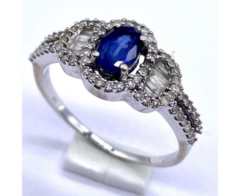 A 9K white gold sapphire and diamond ring set with brilliant cut and baguette cut diamonds, has split to base of ring, size N